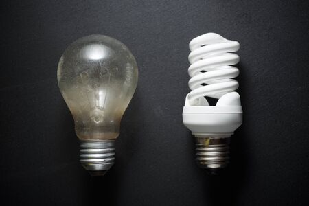 An old incandescent bulb and a modern bulb on a black table.