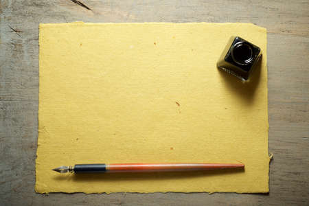 Nib pen for calligraphy and inkwell on a yellow handmade craft paper.
