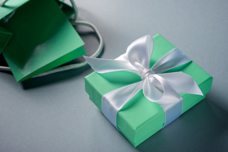 Green gift box with a white ribbon on a tableの写真素材