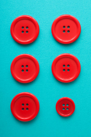 Close-up of six red buttons of different sizes on a green surfaceの写真素材