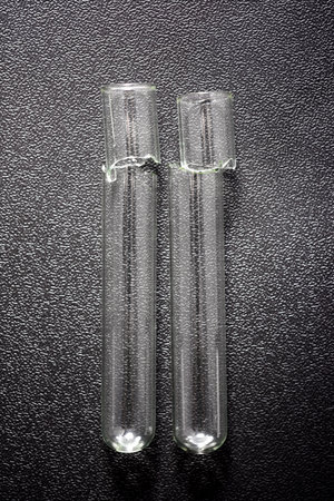 Close up of a pair of broken glass test tubes on a plastic black surfaceの写真素材