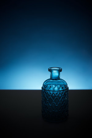 Close up of a blue colored elegant bottle on a black table and backlit.の写真素材