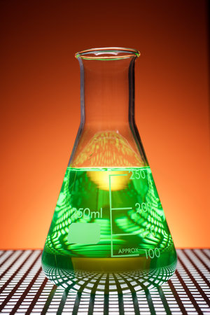 Close up of a glass beaker with green liquid standing in a laboratory countertop and backlit.の写真素材