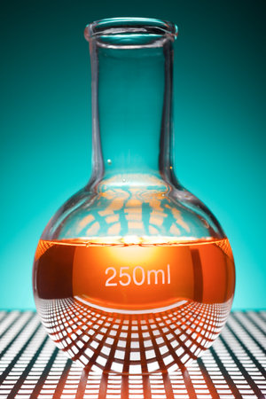 Close up of a glass beaker with orange liquid standing in a laboratory countertop and backlit.の写真素材