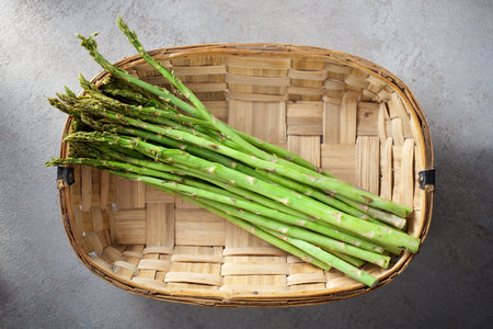 Close up of a bunch of green asparagus in a wicker basket on a kitchen tableの写真素材