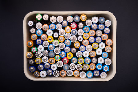 Close-up of a large group of small cylindrical AA batteries in a plastic box on a black table, ready to be recycled.の写真素材