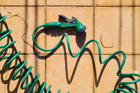 Close-up of a green coiled hose with a spray gun on the floor of a terrace.