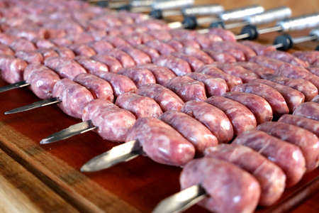 Lots of raw sausage skewers. ready to roast on the barbecue. On a wooden board in the background.の写真素材