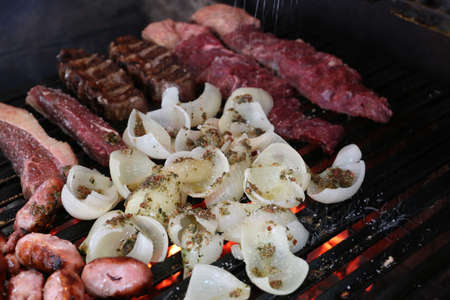 grill full of meats, sausages, onions, and steaks.の写真素材