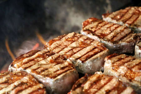 Ancho steak grilled on the grill with glowing charcoal in the background. Many steaks lined up. Side view.の写真素材