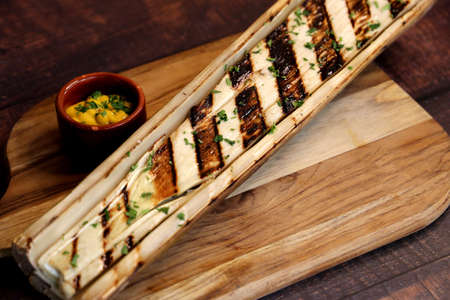 Beautiful whole hearts of palm with barbecue marks on a wooden board with a knife beside it and mustard sauce.の写真素材
