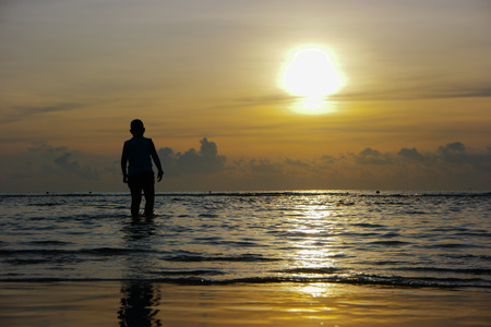 Silhouette of the asian boy standing at the beach during beautiful sunsetの写真素材