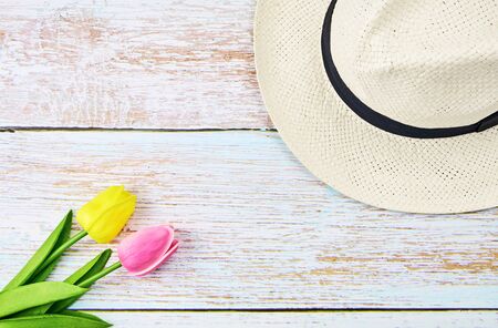 A white straw hat with tulips on a wooden background. Top view,の写真素材