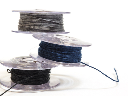 Three plastic spool of threads, gray black and blue color, for sewing machine on a white background