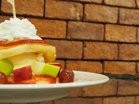 Pancakes with fresh fruits and whipped cream on glass table with red brick wall background.の写真素材