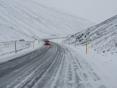 A red car on winter road with mountain on the side of the road covered with snowの写真素材