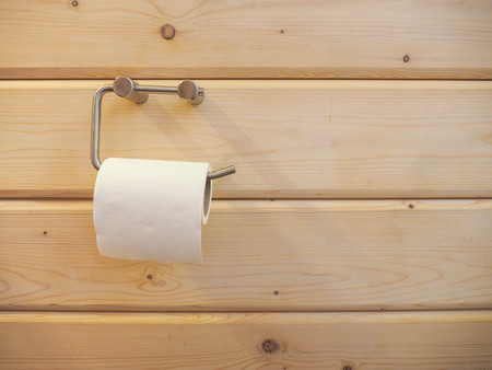 A roll of  toilet paper hanging on a holder with wooden wall.の写真素材