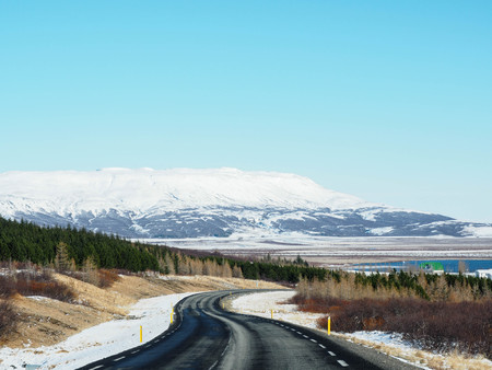 Curved winter asphalt road with trees and mountain on the side of the road covered with snowの写真素材