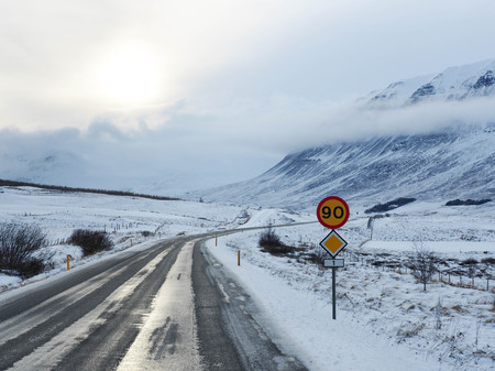 Winter road with mountain on the side of the road covered with snow and a road sign limiting speed.の写真素材