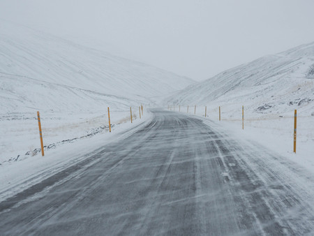 Wind blown snow covered winter road with mountain on the side of the road covered with snowの写真素材