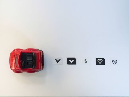 Small paper simulated as a SIM card and a red toy car on white background.  Dollar, wifi and heart...