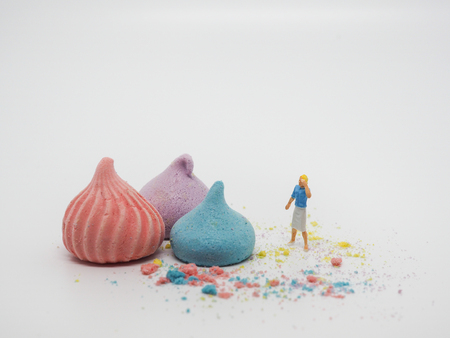 Miniature woman standing near sweets and thinking of sugar, diet, fat and diabetes. Colorful merengue on white background, selective focus. Health care conceptの写真素材