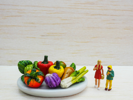 Miniature children standing near a dish of vegetable on wooden background.の写真素材