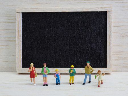 Miniature children standing in front of a blackboard on wooden background. Back to school concept.の写真素材