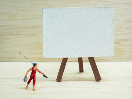 Miniature little boy standing near an easel on wooden background. Back to school concept.の写真素材