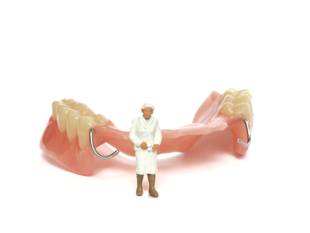 Miniature elderly standing on removable denture, on white background. Dental health concept.