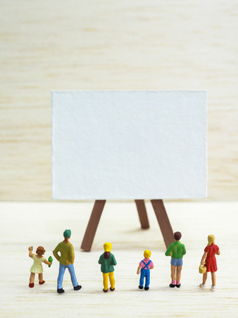 Miniature children standing in front of an easel on wooden background. Back to school conceptの写真素材