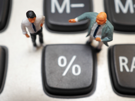 Miniature businessman standing on calculator and thinking of percent profit and money management. Business money and financial concept.の写真素材