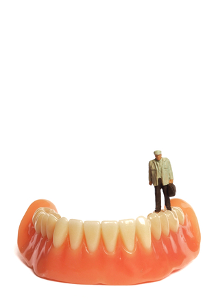 Miniature elderly standing on removable denture, on white background. Dental health concept.の写真素材