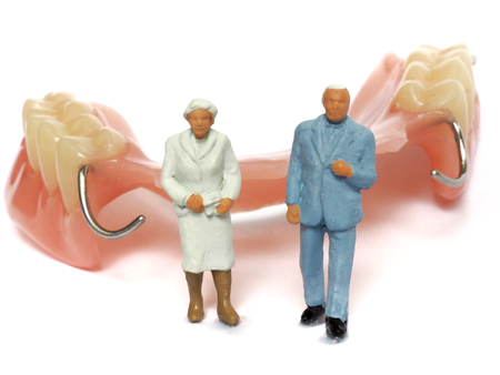 Miniature elderly couple standing on removable denture, on white background. Dental health conceptの写真素材