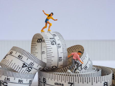 Miniature woman skating on measuring tape, thinking of weight loss and slim body. Healthy lifestyle concept.の写真素材