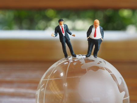 Miniature businessman stand on globe of glass with wooden background. Business and idea conceptの写真素材