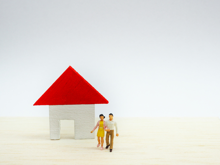 Miniature couple standing in front of small house on wooden background. couple and life planning conceptの写真素材
