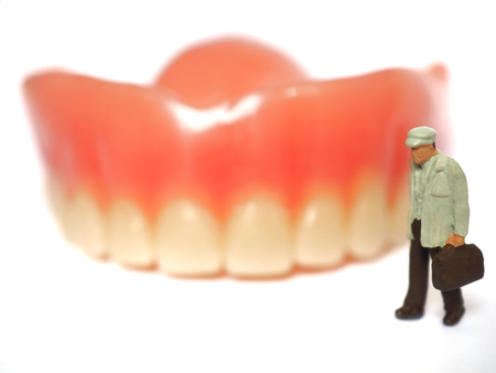 Miniature elderly standing on removable denture, on white background. Dental health concept.の写真素材