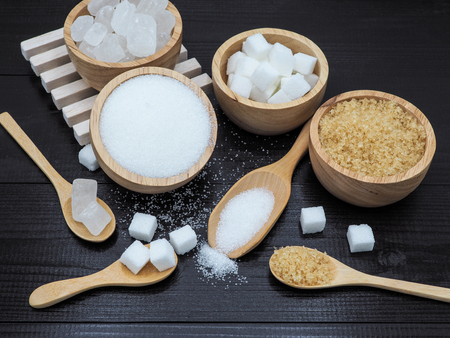 Wooden bowl and spoon with sugar cube on dark wood background.の写真素材
