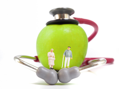 Miniature senior couple, small figures, standing on stethoscope and green apple. Health care and healthy lifestyle concept.の写真素材