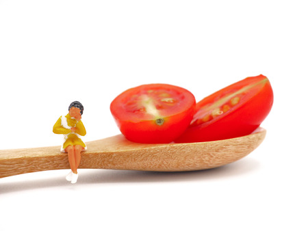 Miniature woman sitting on fresh grape or cherry tomato with wooden spoon, thinking of weight loss and slim body. Healthy lifestyle concept. white background.の写真素材