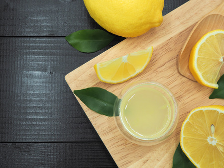 Fresh lemon juice in small bowl and lemon slice on dark wood backgroundの写真素材
