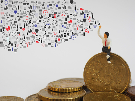 Miniature businessman sitting on Euro coin and drawing business icons on white background. Business and finance conceptの写真素材