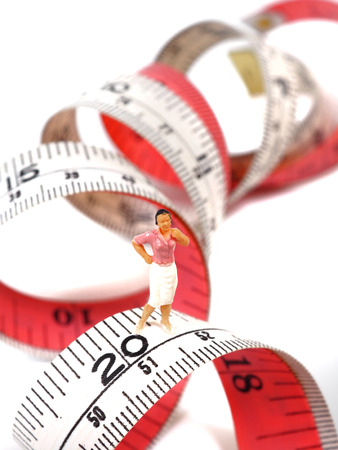 Miniature woman standing near measuring tape, thinking of weight loss and slim body. Healthy lifestyle concept.の写真素材