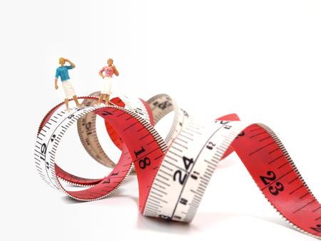 Miniature woman standing near measuring tape, thinking of weight loss and slim body. Healthy lifestyle concept.の写真素材