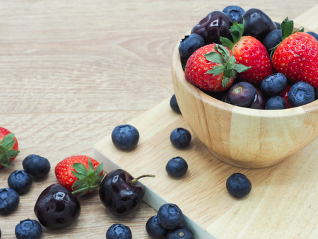 Fresh summer fruits, Cherry, strawberry and blueberry in wooden bowl isolated on wood background.の写真素材