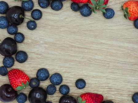 Fresh summer fruits, Cherry, strawberry and blueberry in wooden bowl isolated on wood background.の写真素材