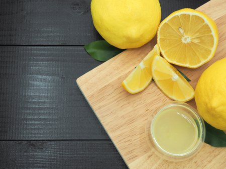 Fresh lemon juice in small bowl and lemon slice on dark wood backgroundの写真素材