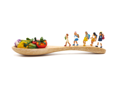 Miniature children on wooden spoon with small vegetables on white background.の写真素材