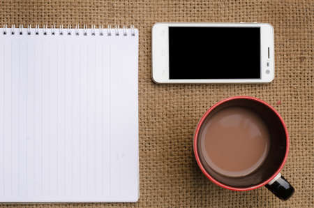 The note book and paper writing set with smart phone and a cup of coffee ,on sackcloth background